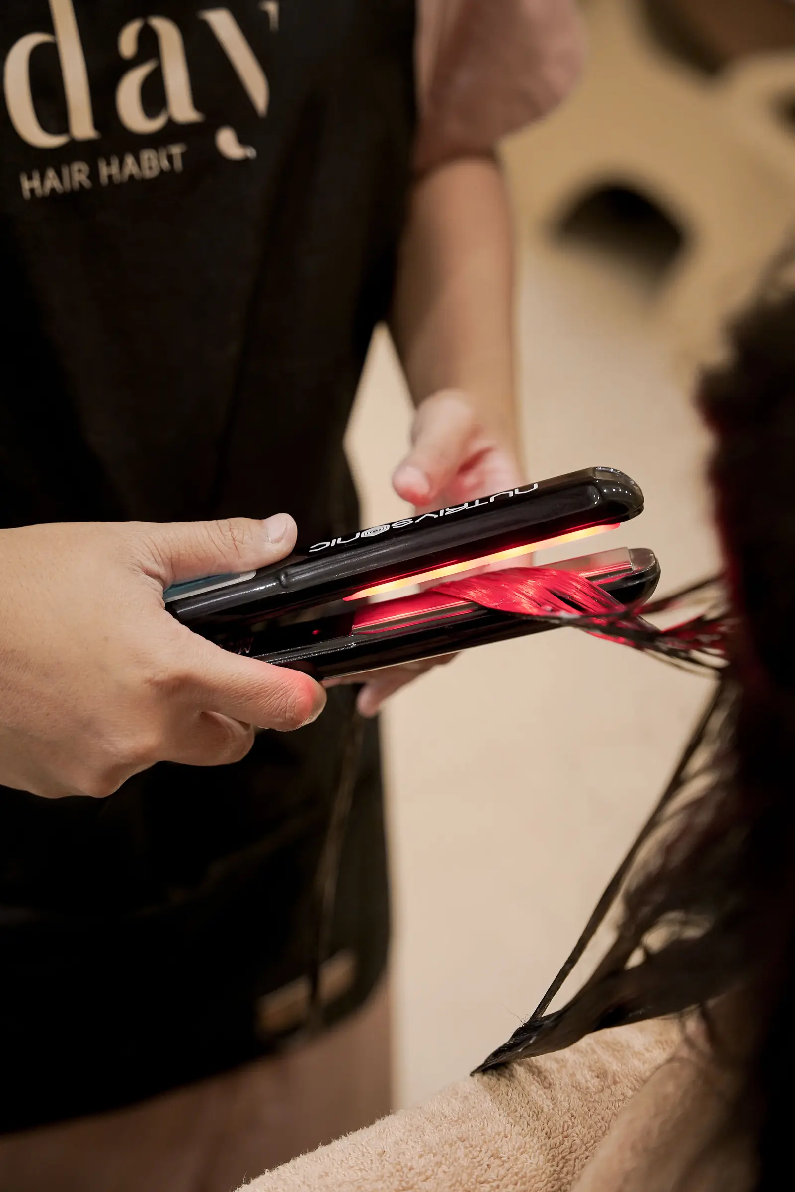 An infrared flat iron smoothing a section of hair at Day Hair Habit