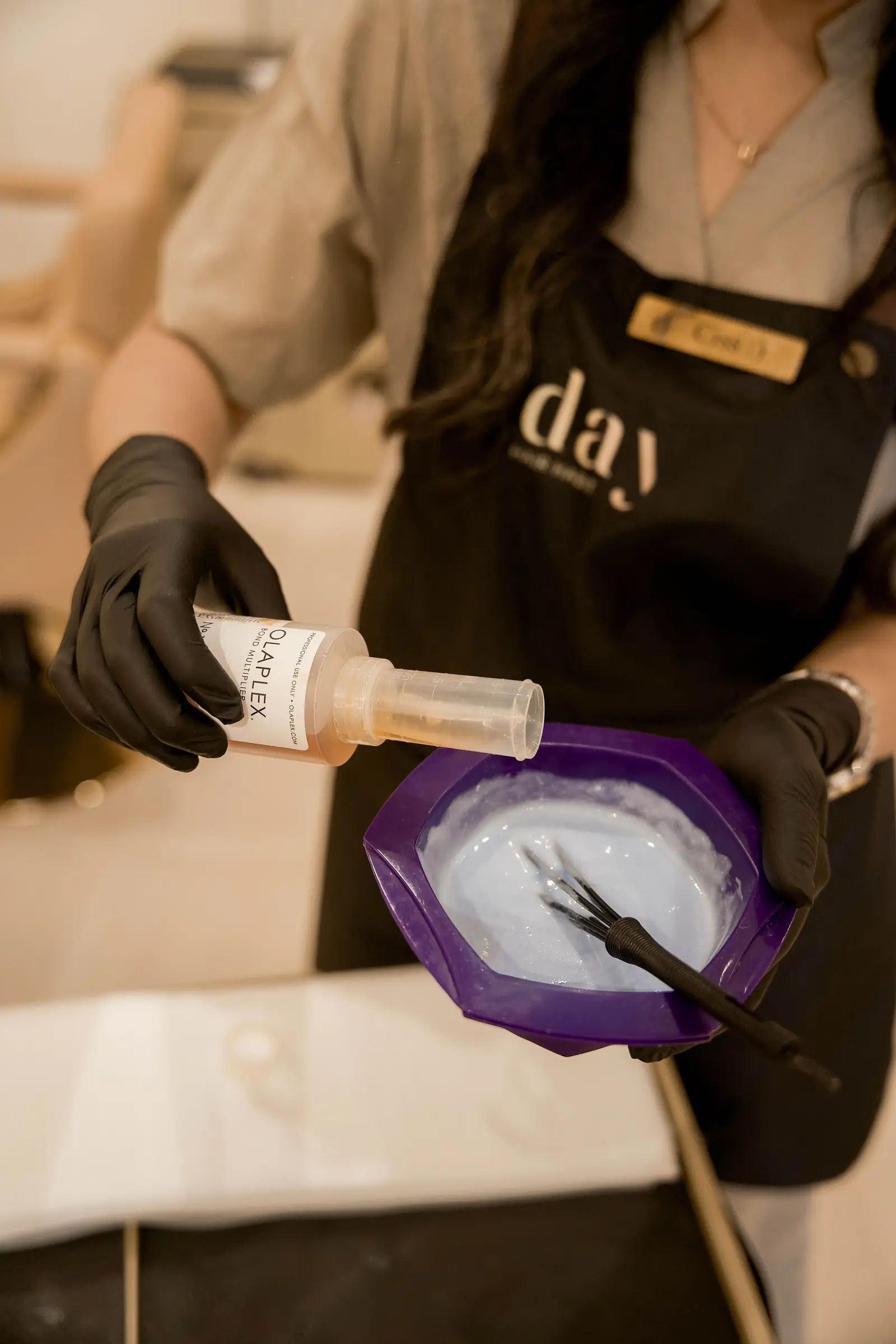 A stylist in a Day Hair Habit apron pouring Olaplex bond multiplier into the color bowl